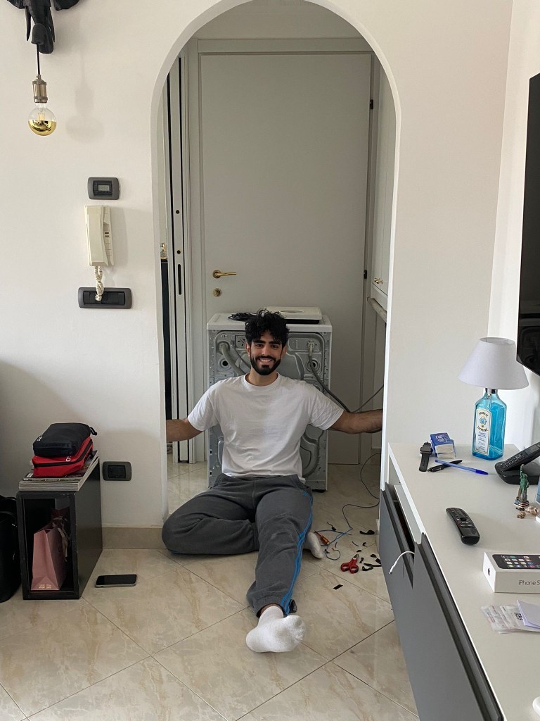Seduto sul pavimento di casa in Italia mentre riparo una lavatrice, con gli attrezzi sparsi intorno